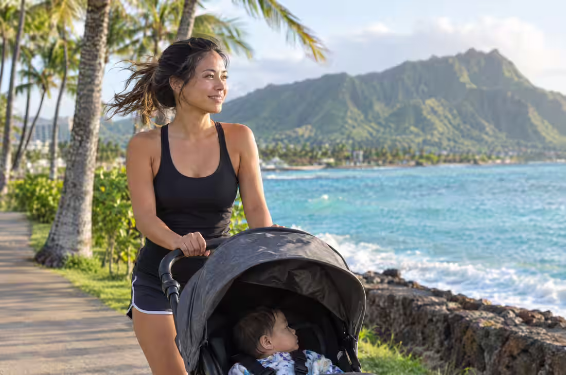 A mother jogging with a stroller along the Oahu coast, Diamond Head behind her