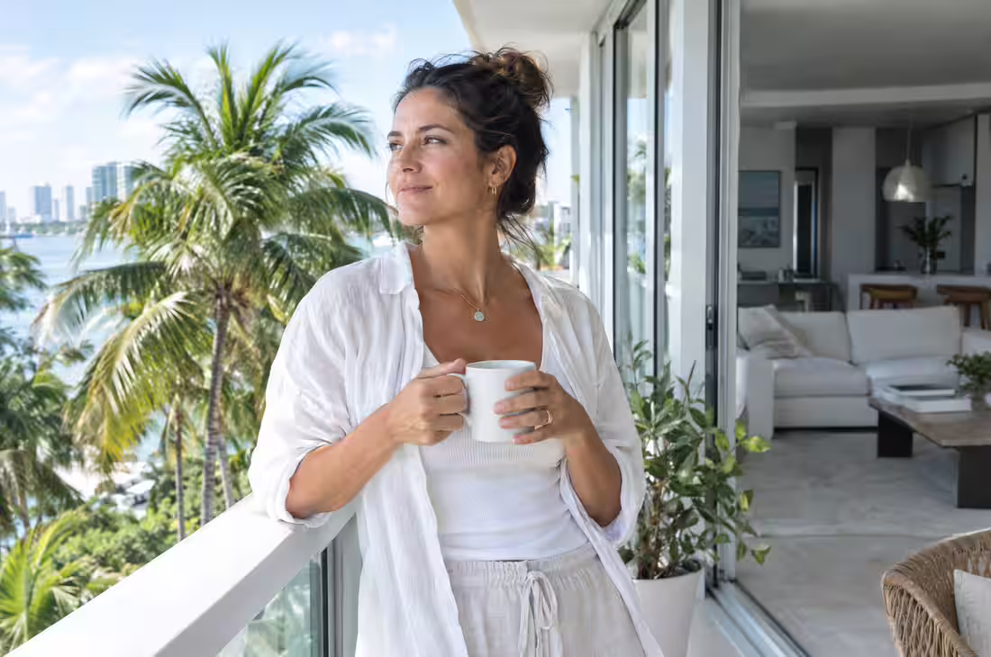 A woman with a cup of coffee on a Miami balcony among palm trees