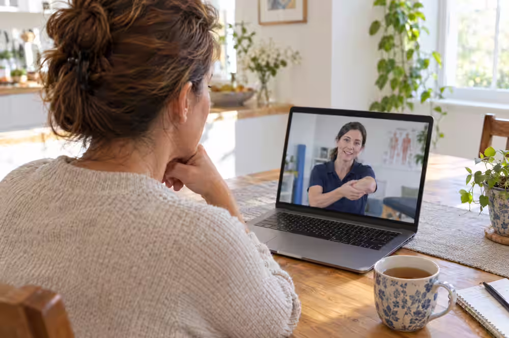 A woman at her kitchen table on a video visit with her physical therapist